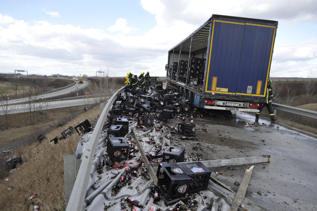 Tűzoltók takarítják fel és pakolják egy sörszállító kamion leborult rakományát az M0-ás autóútról az M4-es autópályára vezető felhajtónál Budapest határában 2020. február 27-én.