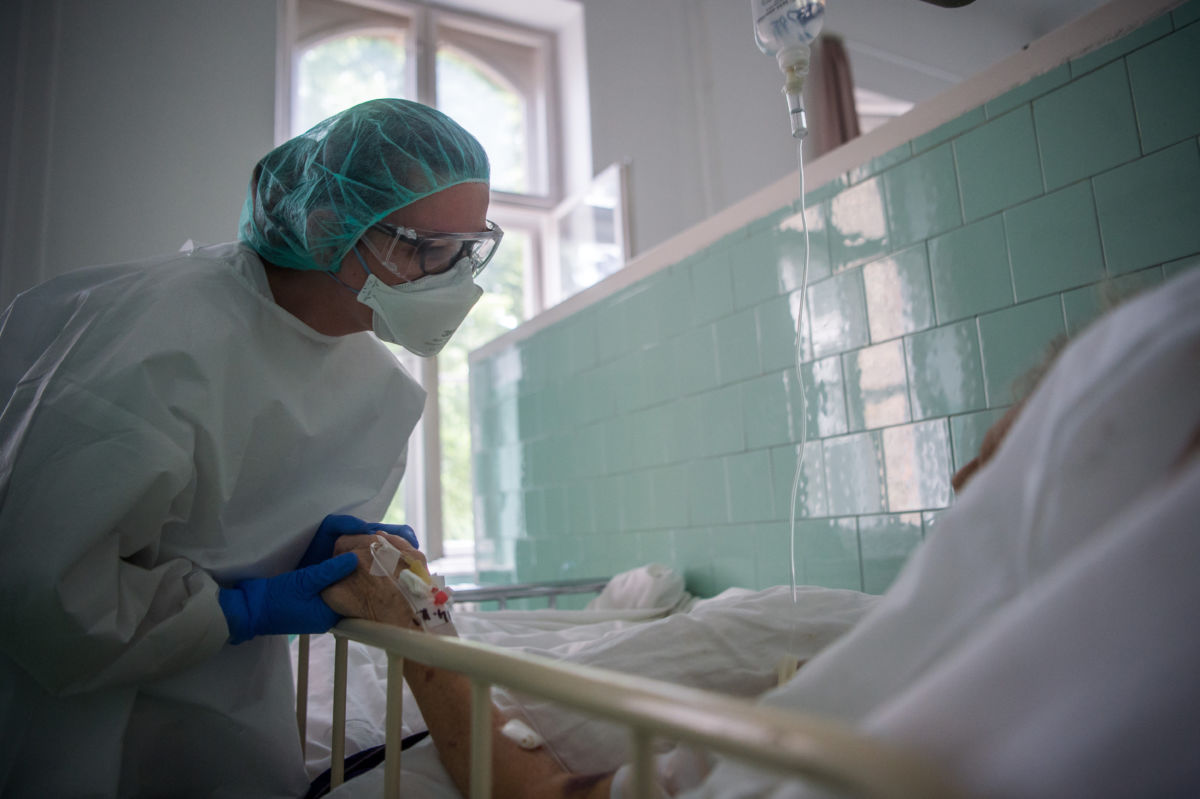 Védőfelszerelést viselő ápoló megsimogatja egy beteg kezét a koronavírussal fertőzött betegek fogadására kialakított Covid Ortopéd-Traumatológiai Osztályon a fővárosi Szent János Kórházban 2020. május 14-én.